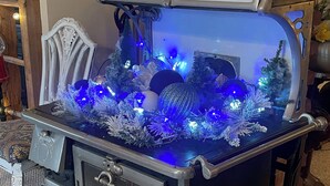 Un poêle de style vintage, agrémenté d’un décor sur le dessus représentant un sapin de Noël et illuminé de lumières bleues.