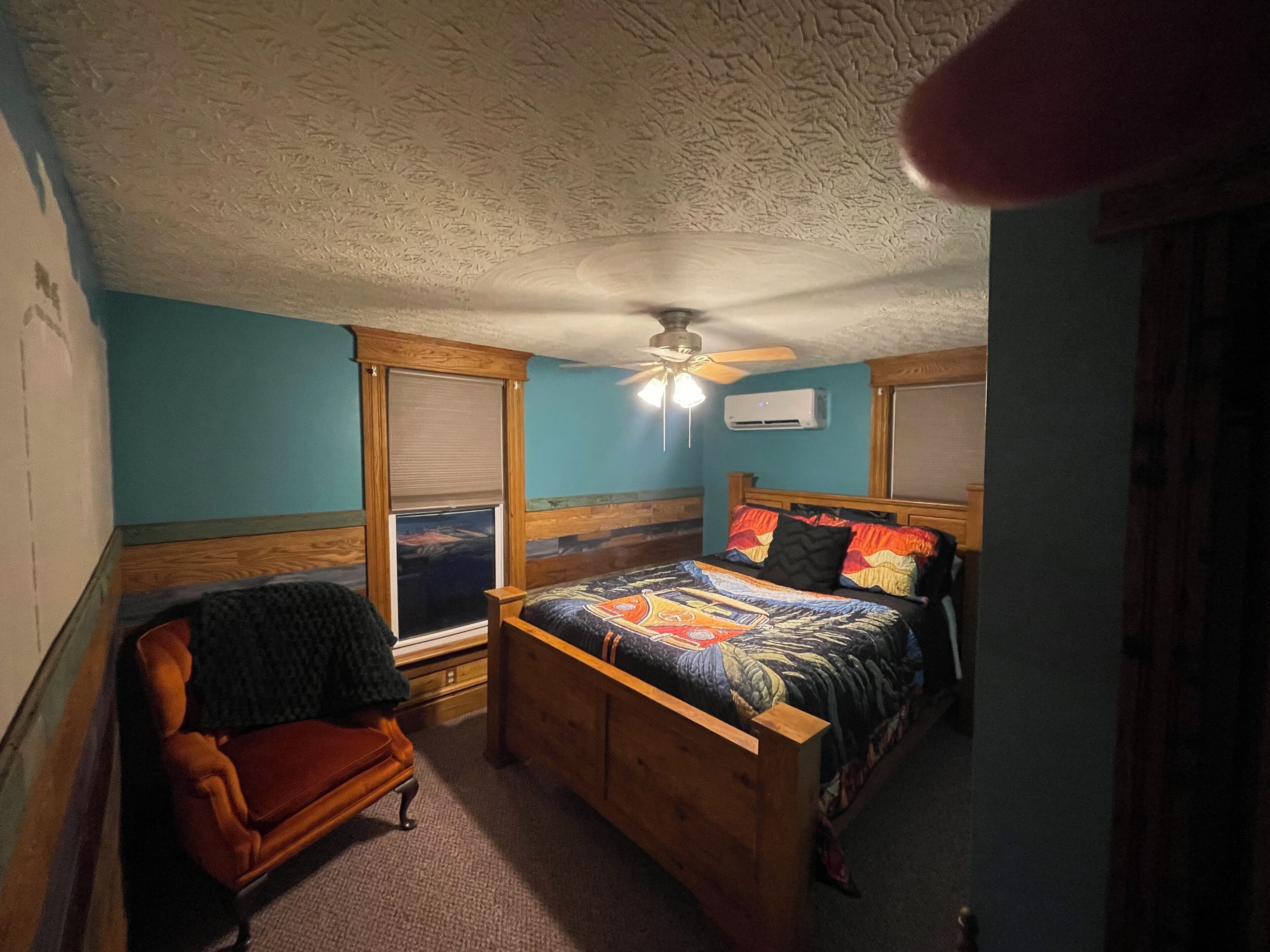 A bedroom with a wooden bed, a chair, a ceiling fan, and a window.