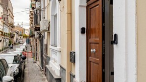 Une rue étroite, bordée de voitures garées, et un bâtiment doté d’une porte en bois et d’une fenêtre en arc de cercle.