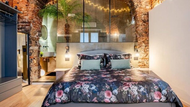 Une chambre à coucher comprenant un lit, une table de chevet, un miroir et une grande fenêtre donnant sur un arbre.