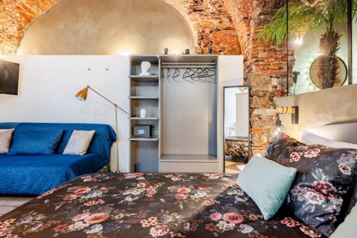 A bedroom with a bed, a blue sofa, a wardrobe, and a brick wall.