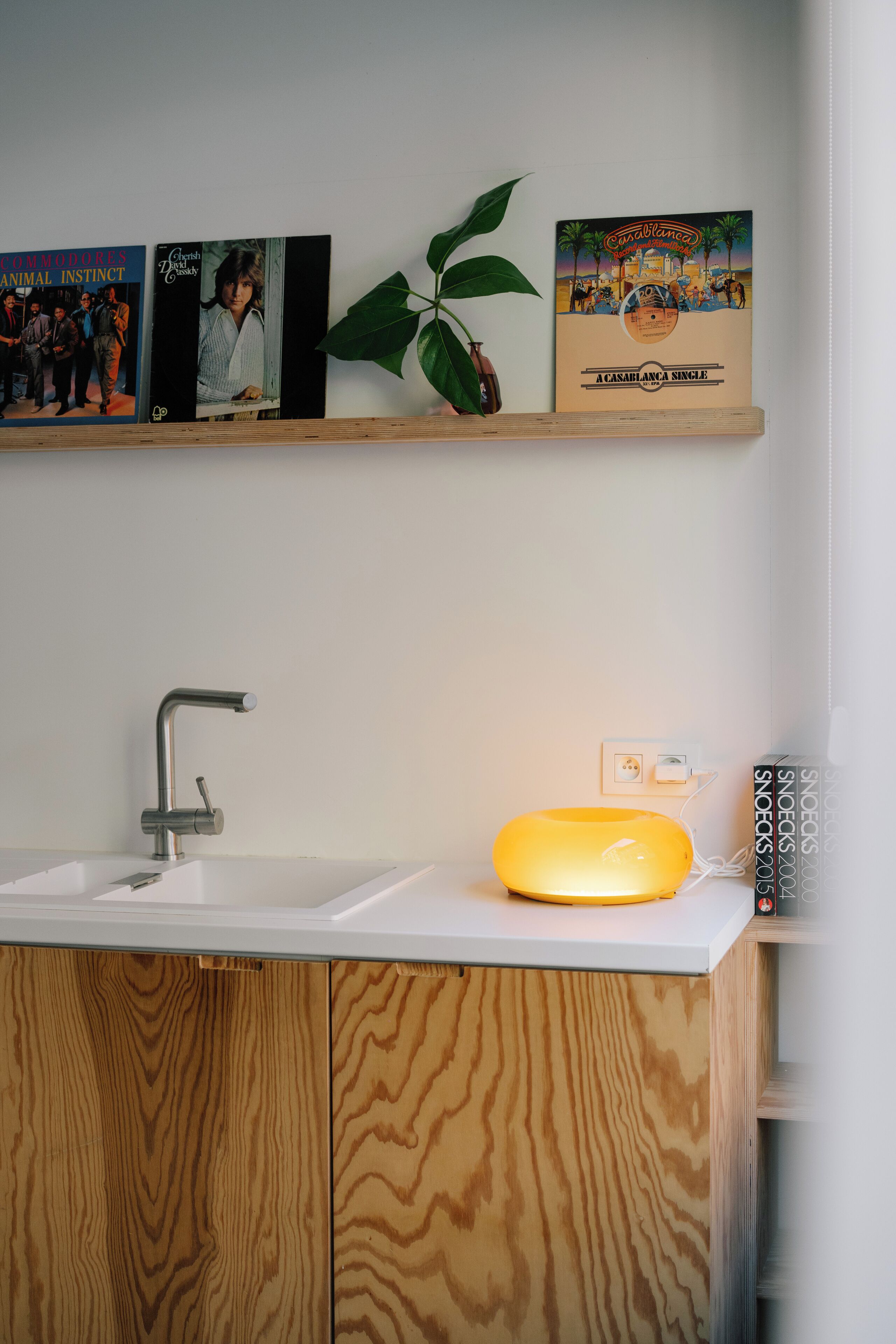 A bathroom with a wooden vanity, a modern faucet, and a shelf with framed pictures and a plant.