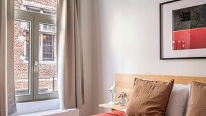 A hotel room with a bed, a nightstand, a lamp, and a framed picture on the wall. - A Place - Leeuwenstraat 15 (Antwerp)