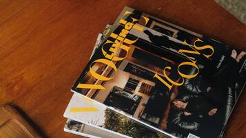 A stack of magazines on a wooden table, accompanied by a small potted plant and two ceramic vases.