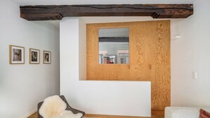 A room with a wooden ceiling beam, a white reception desk, a wicker chair with a fluffy cushion, a white sofa, and three framed pictures on the wall. - A Place - Leeuwenstraat 15 (Antwerp)