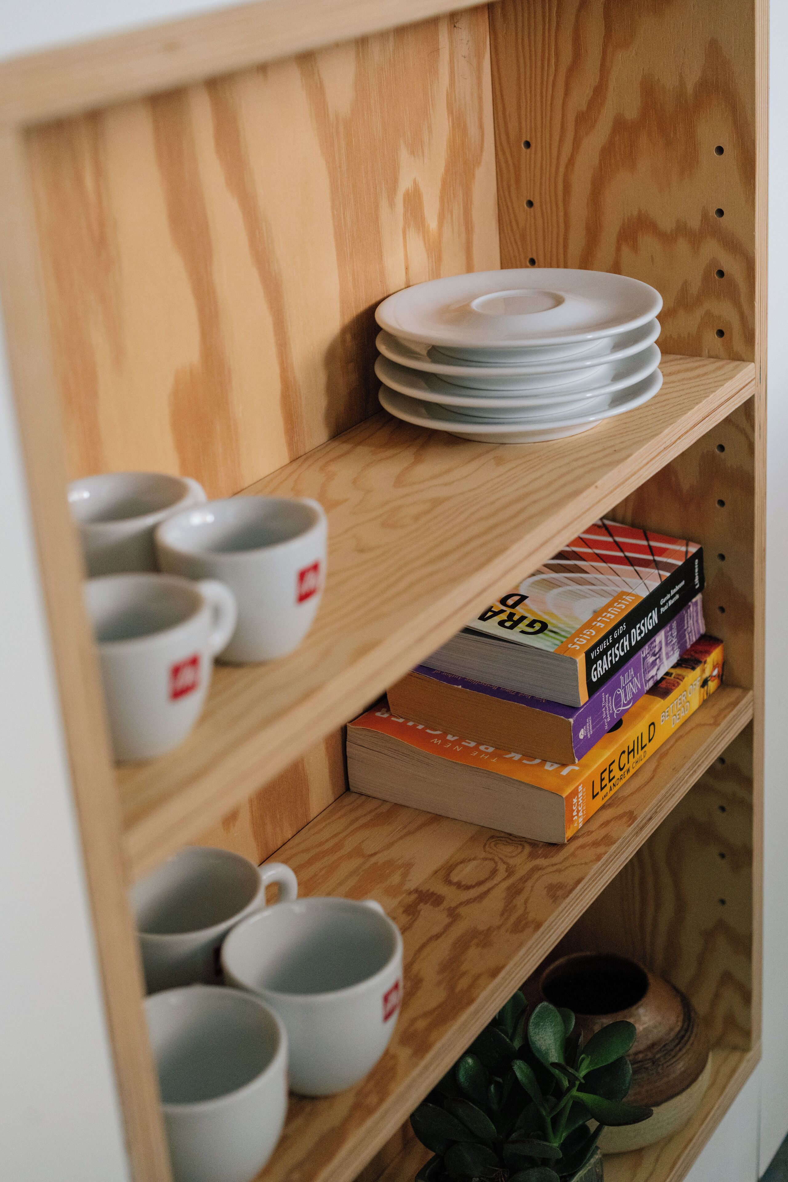 A wooden shelf with white mugs, stacked plates, and books.