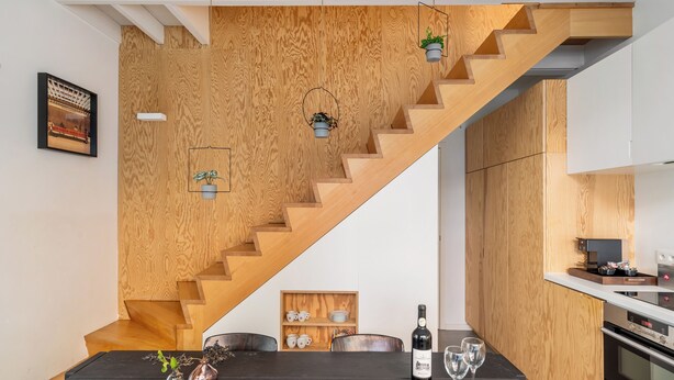 A modern kitchen with wooden accents, a dining area with a dark table, and a staircase with wooden steps. - A Place - Leeuwenstraat 15 (Antwerp)