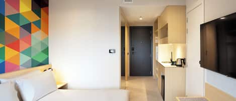 A hotel room with a bed, a TV, a kitchenette, and a colorful geometric wall design.