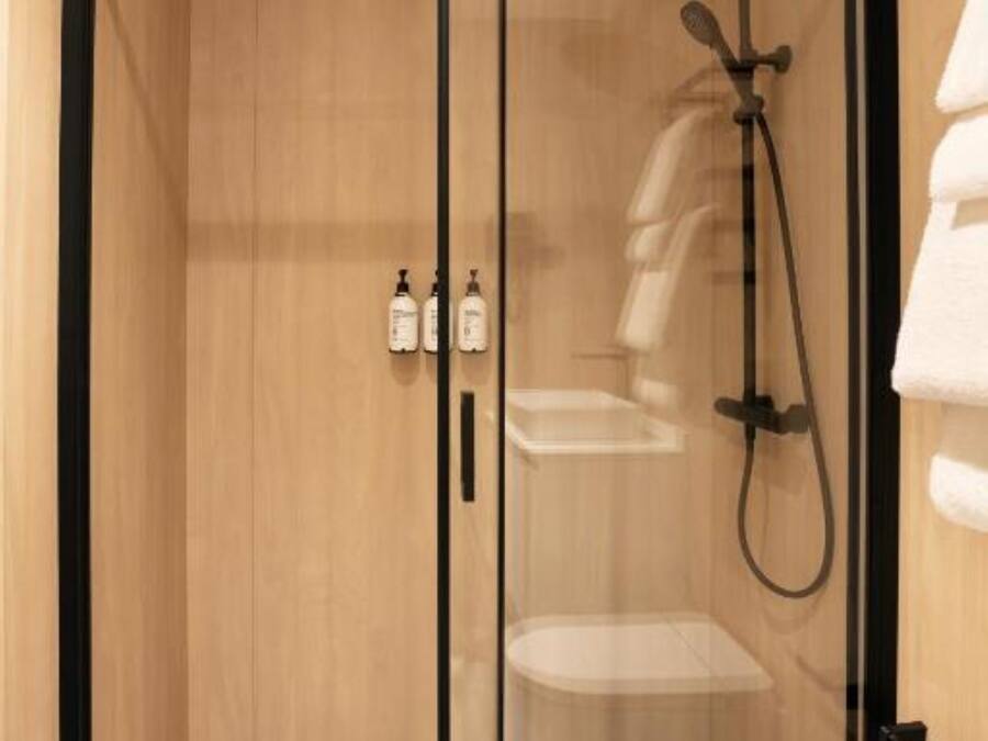 Un baño moderno con mampara de vidrio, paredes de madera y un perchero para toallas.