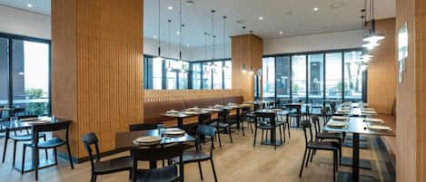 A modern dining area with wooden paneling, black chairs, and tables arranged for groups.