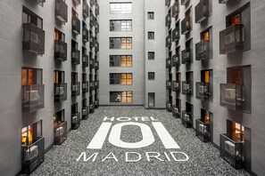 Een modern hotelinterieur met een centrale hal, meerdere balkons en een bordje met de tekst 'HOTEL 101 MADRID'.