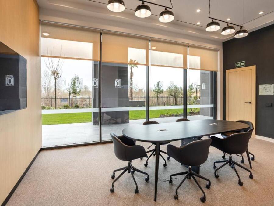 Een vergaderruimte met een grote tafel, vier stoelen en een deur met de tekst 'SALIDA'.