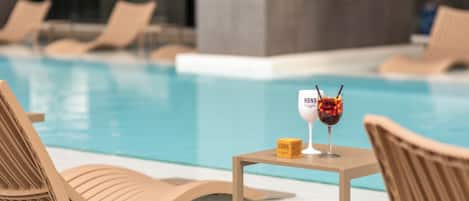 A poolside area with lounge chairs and a table with a drink and a bottle.