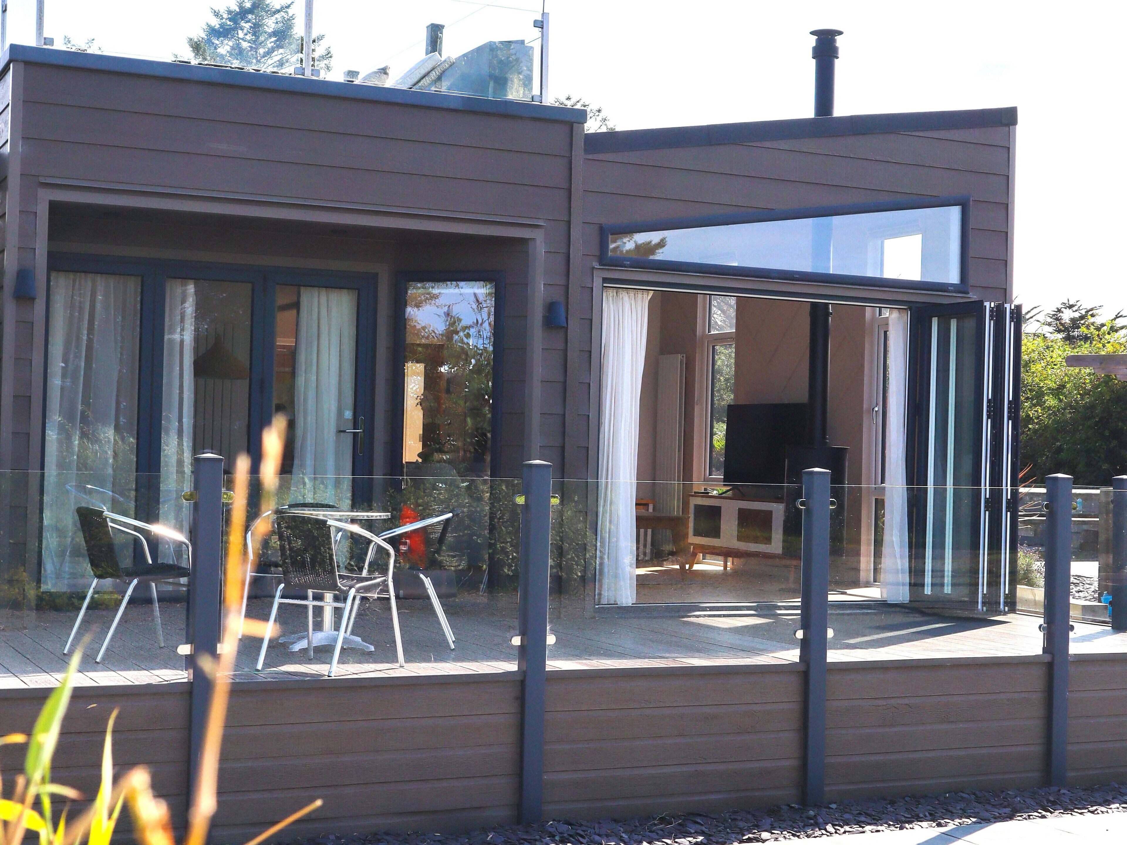 Un edificio moderno con grandes puertas y ventanas de vidrio, un patio con mobiliario exterior y una chimenea visible.