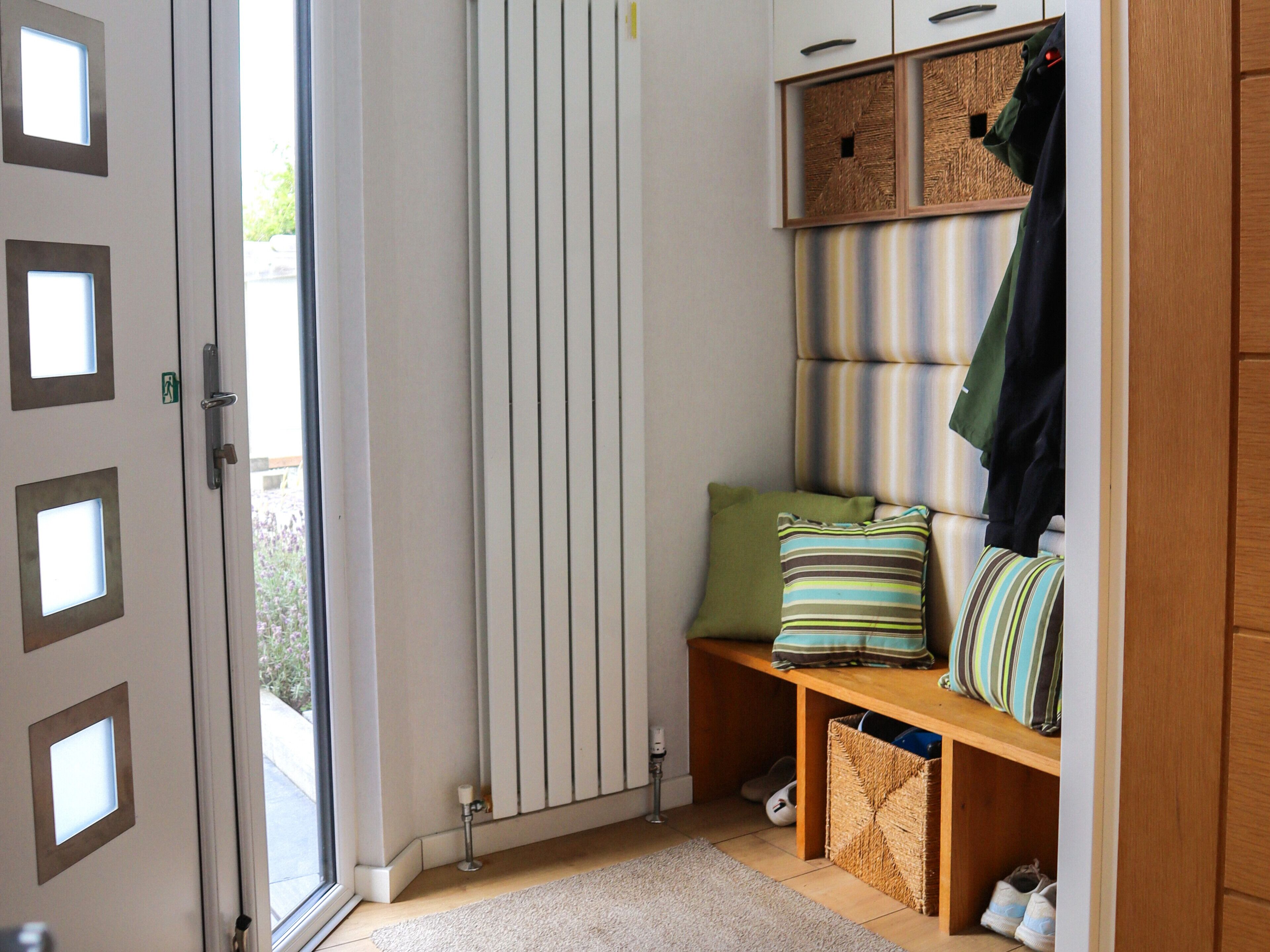 A room with a sliding door, a bench with pillows, a coat rack, and a shoe storage area.