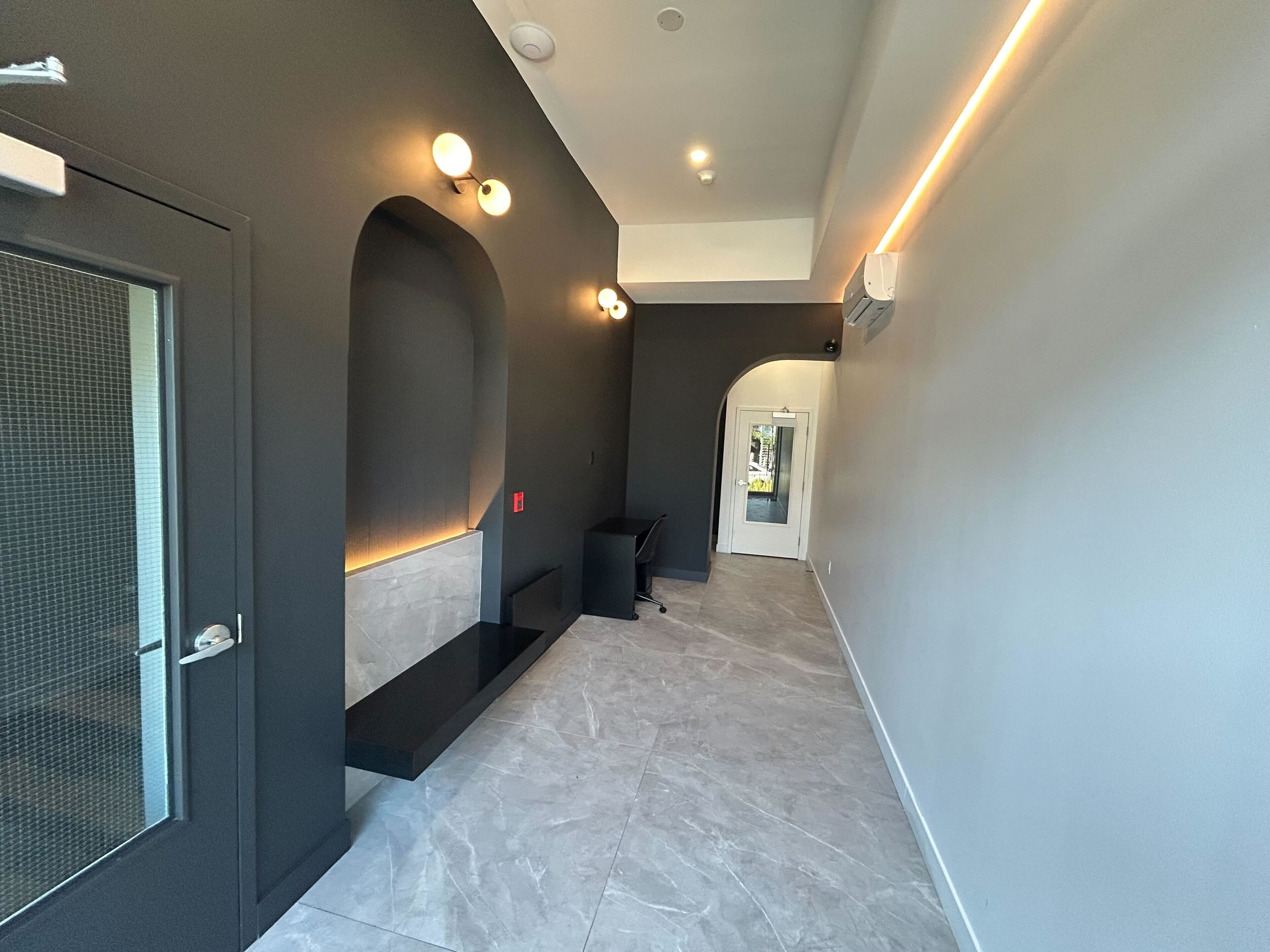 A modern hallway with a dark wall, a recessed seating area, and a door with a mesh screen.