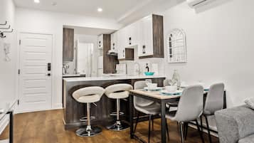 Una cocina moderna con armarios blancos, encimera de madera y una zona de comedor con sillas grises y una mesa de madera.