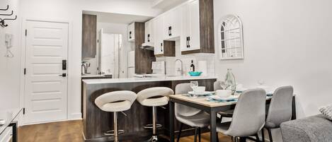 A modern kitchen with white cabinets, a wooden countertop, and a dining area with grey chairs and a wooden table.