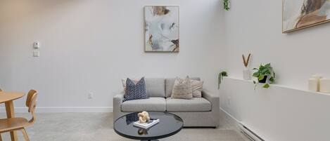 A modern living room with a grey sofa, a round black coffee table, and a painting on the wall.