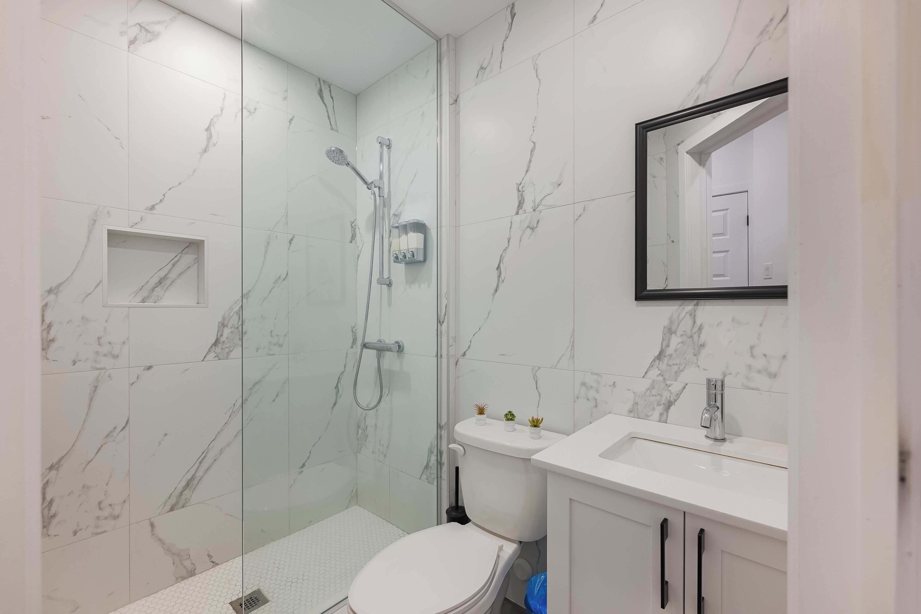 Ein modernes Badezimmer mit einer Duschkabine aus Glas, einer weißen Toilette und einem Waschbecken mit Spiegel darüber.