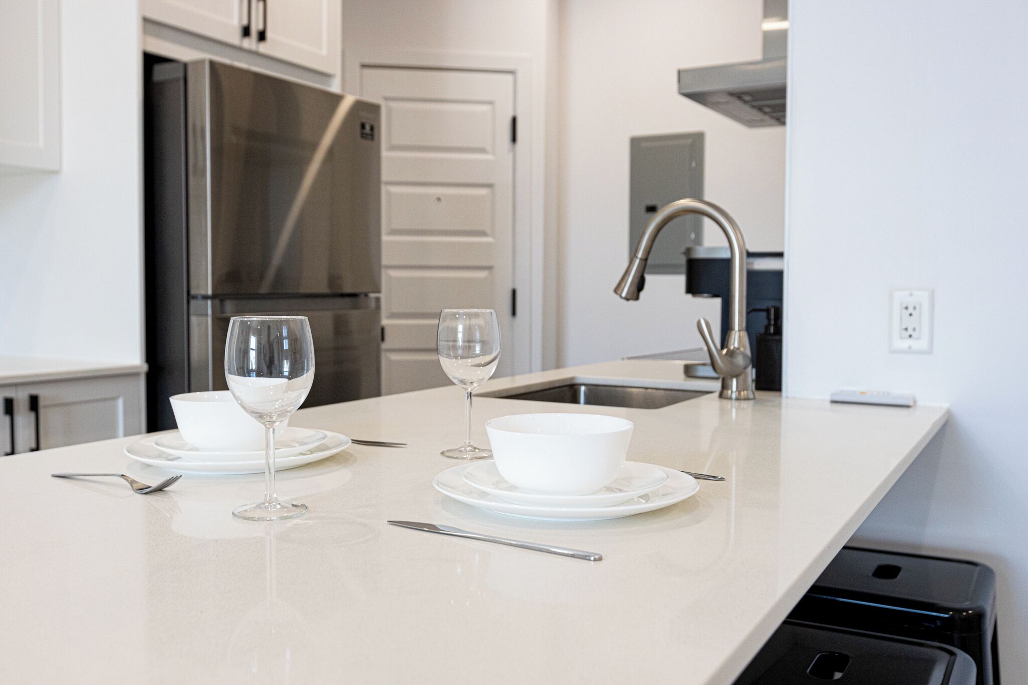 Una cocina moderna con un refrigerador de acero inoxidable, una encimera blanca y un lavamanos.