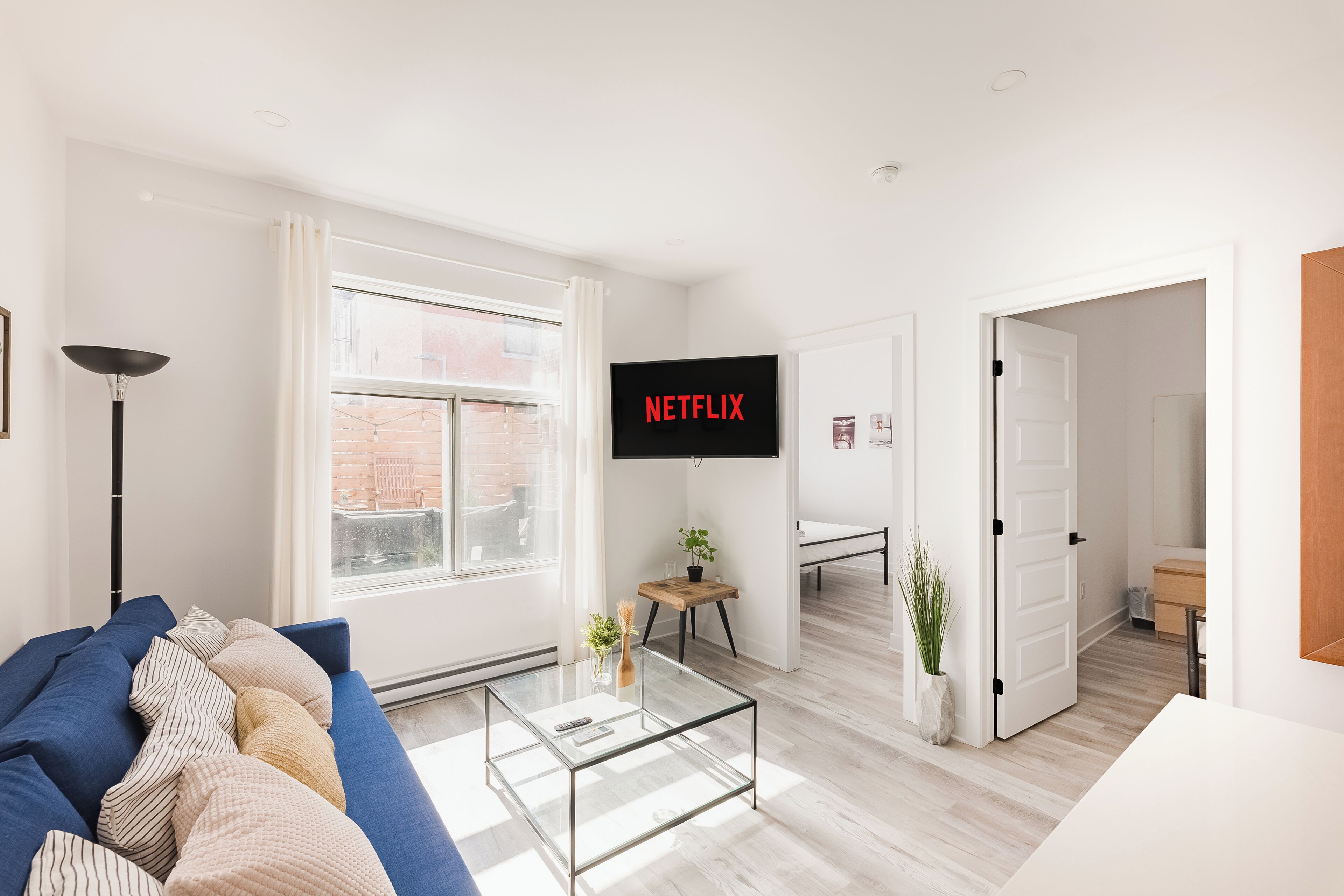 A modern living room with a blue sofa, a glass coffee table, and a TV displaying "NETFLIX".