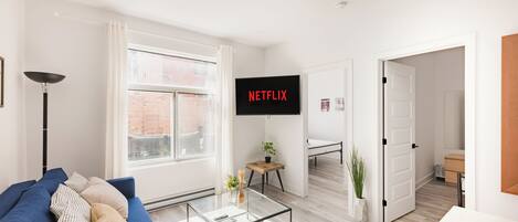 A modern living room with a blue sofa, a glass coffee table, and a TV displaying "NETFLIX".