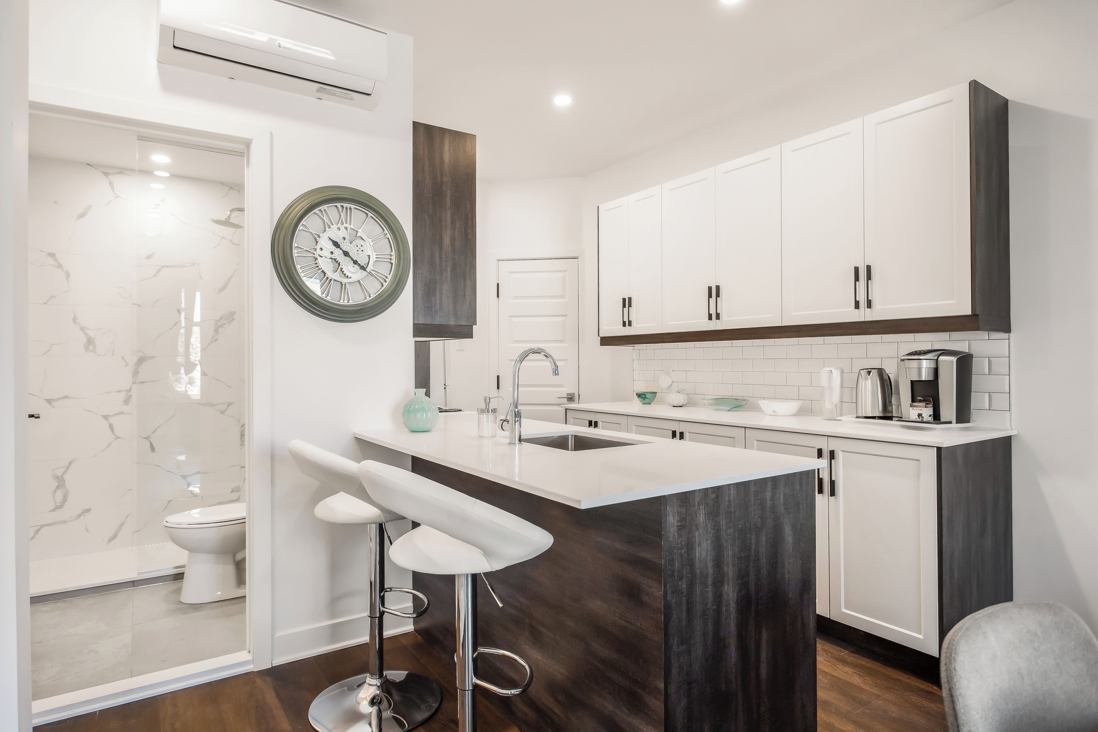 Une cuisine moderne avec des meubles blancs, un îlot central en bois foncé et une grande horloge au mur.