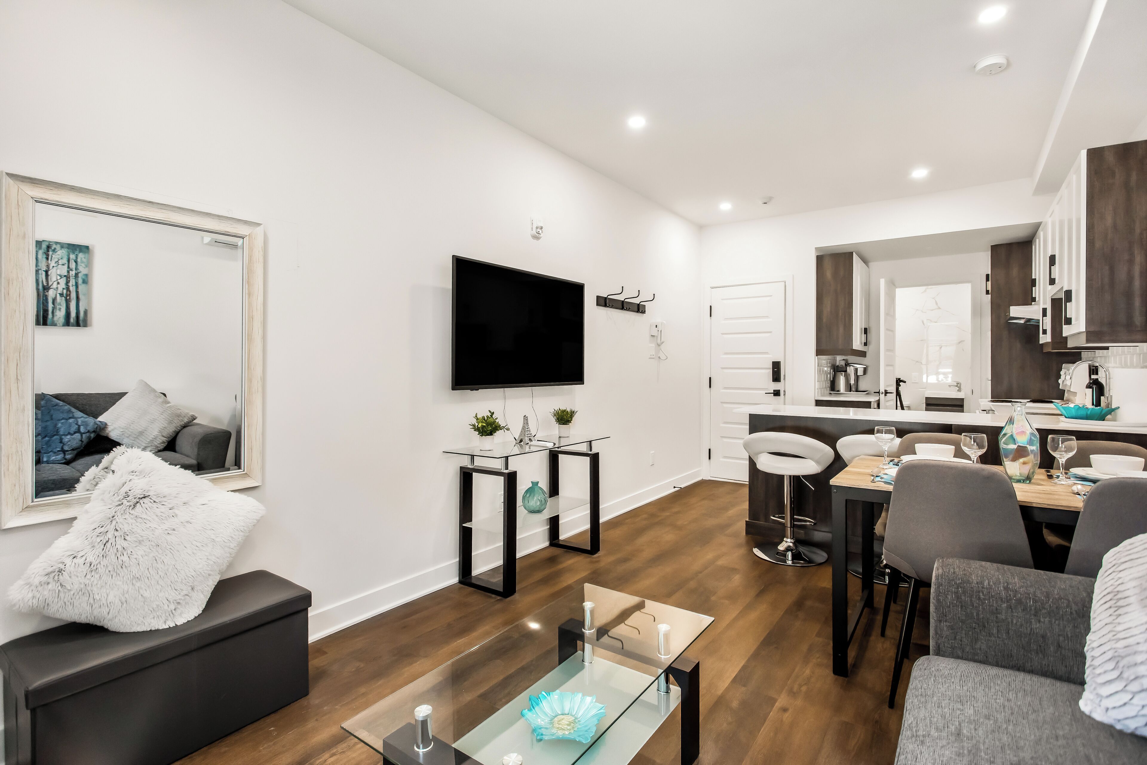 A modern living room with a flat-screen TV, a glass coffee table, and a dining area with a wooden table and chairs.