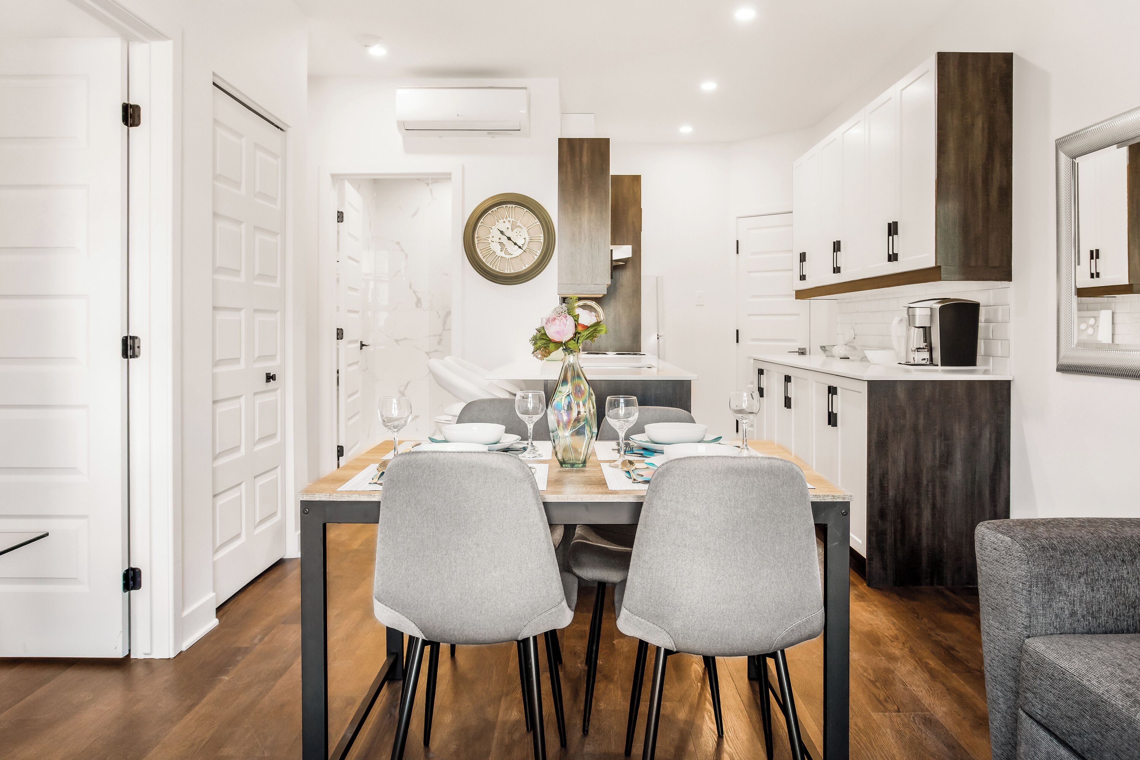 Cocina moderna con armarios blancos, una pared de acento de madera y un comedor con mesa dispuesta para cuatro.