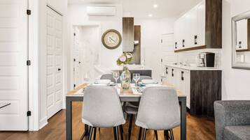 Cocina moderna con armarios blancos, una pared de acento de madera y un comedor con mesa dispuesta para cuatro.