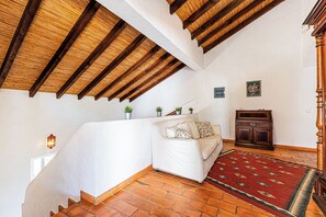 Une pièce avec un canapé blanc, un tapis à motifs rouges, un meuble en bois et un escalier doté d’un plafond en bois.