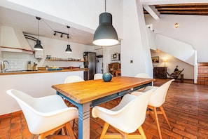A modern kitchen with a wooden table and white chairs, a hanging light fixture, and a brick floor. - Monte Labarito - Casa Petra - Country House 30' away from the beach. (Reliquias)