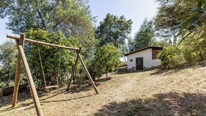 Un conjunto de columpios de madera en un área cubierta de césped, con un edificio pequeño al fondo.