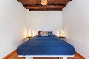 A bedroom with a wooden ceiling, white walls, a blue bedspread, and two bedside tables with lantern-style lamps. - Monte Labarito - Casa Petra - Country House 30' away from the beach. (Reliquias)
