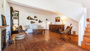 Amplia sala de estar con suelo de ladrillo, chimenea, estantería, sofá, mesa de centro y una guitarra.