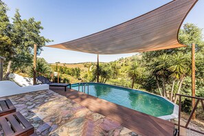 Une piscine dotée d’une terrasse en bois, d ’un revêtement de sol en pierre et d’un auvent offrant de l’ombre.