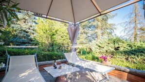 Ein Sitzbereich im Freien mit zwei Lounge-Stühlen und einem Tisch, umgeben von üppigem Grün und freiem Blick zum Himmel.