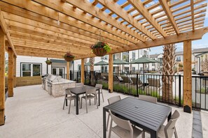 Eine Terrasse im Freien mit einer Holz-Pergola, Sitzgelegenheiten, einem Grillplatz und hängenden Blumenkörben.
