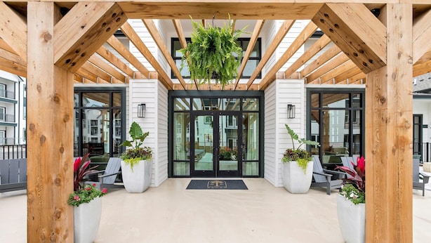 A wooden pergola entrance with a hanging plant, large glass doors, and potted plants on either side. - Global Luxury Suites Downtown Charleston (North Charleston)