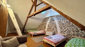A cozy attic bedroom with a sloped ceiling, two single beds, a wooden chair, and a stone wall. - Large family home with extensive grounds (Tortebesse)