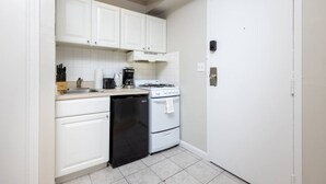 A compact kitchen with white cabinets, a stove, a dishwasher, and a coffee maker. - Back Bay Studio with Exposed Brick (Boston)