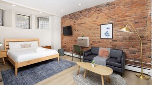 A modern bedroom with a brick wall, a bed, a sofa, a coffee table, and a TV mounted on the wall. - Back Bay Studio with Exposed Brick (Boston)