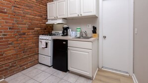 A compact kitchen with white cabinets, a gas stove, a dishwasher, and a coffee maker. - Serene Studio with Cozy Atmosphere (Boston)