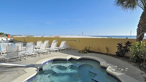 Un bain Ă remous Ă bords incurvĂ©s, entourĂ© de chaises longues et dâune piscine, avec une vue sur la plage en arriĂšre-plan.