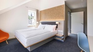 Ett modernt hotellrum med en säng, ett skrivbord och en stol.
