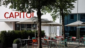 Ett utomhusområde med bord och stolar framför en byggnad med en stor skylt där det står "CAPITOI".