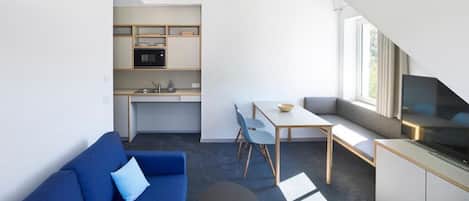 Un espacio habitable compacto con kitchenette, sofá, comedor y televisor.