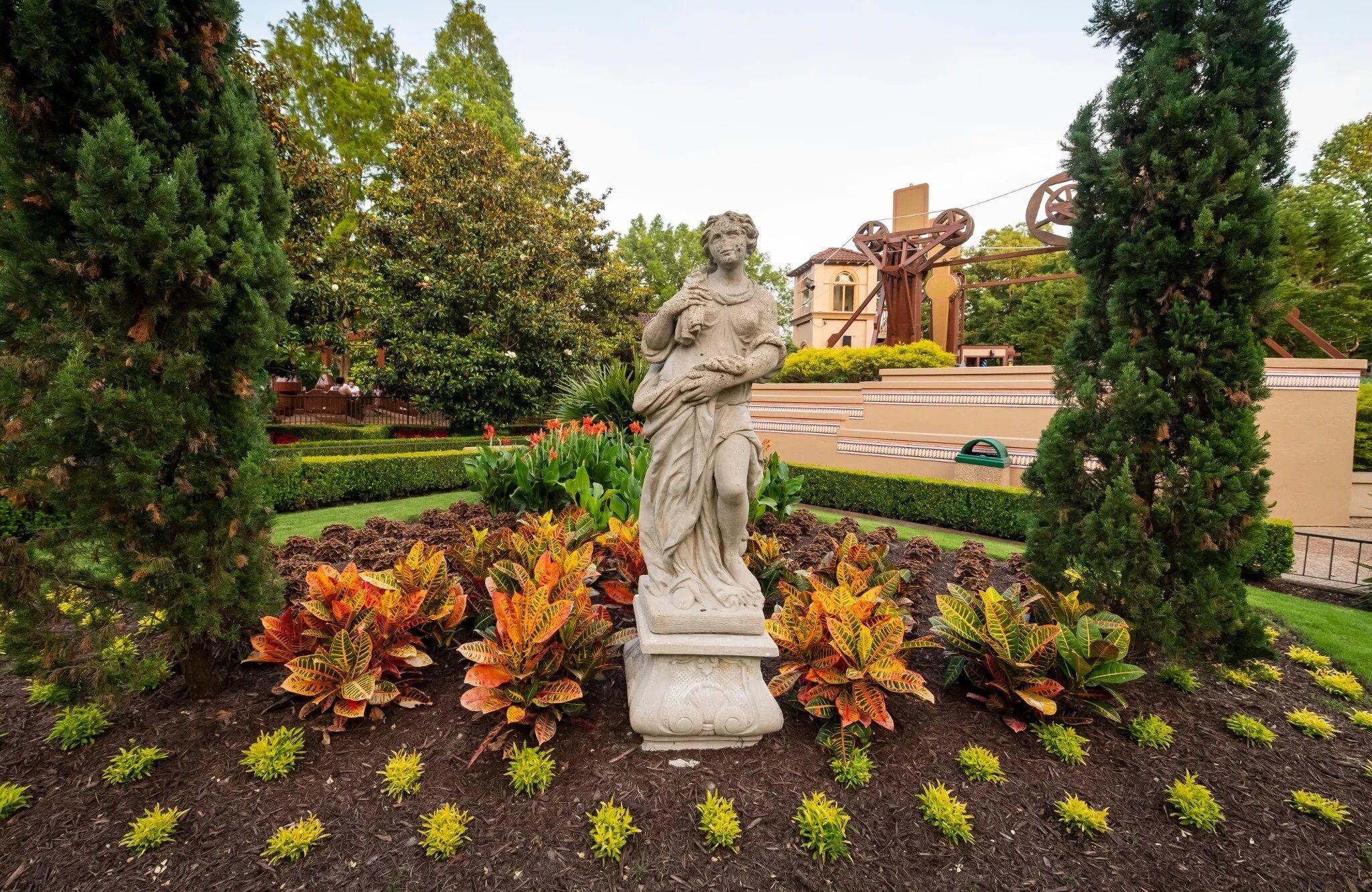 Un jardin agrémenté d’une statue, de haies soigneusement taillées et d’une grande variété de plantes.