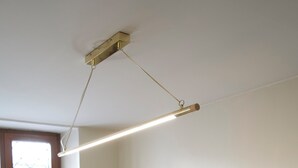 Een keuken met houten kastjes, een betegelde spatwand, een raam met kantgordijnen en een hanglamp.